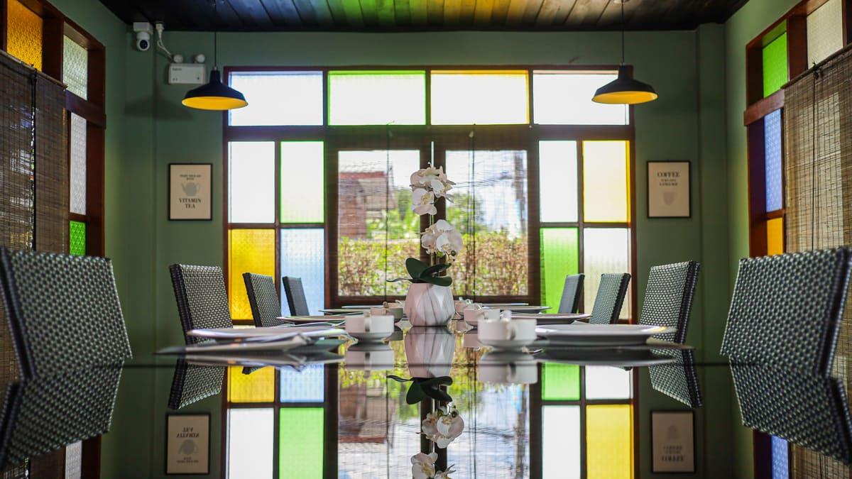 Dining room with one shared glass table, ten chairs and stained glass windows at a Thailand rehab