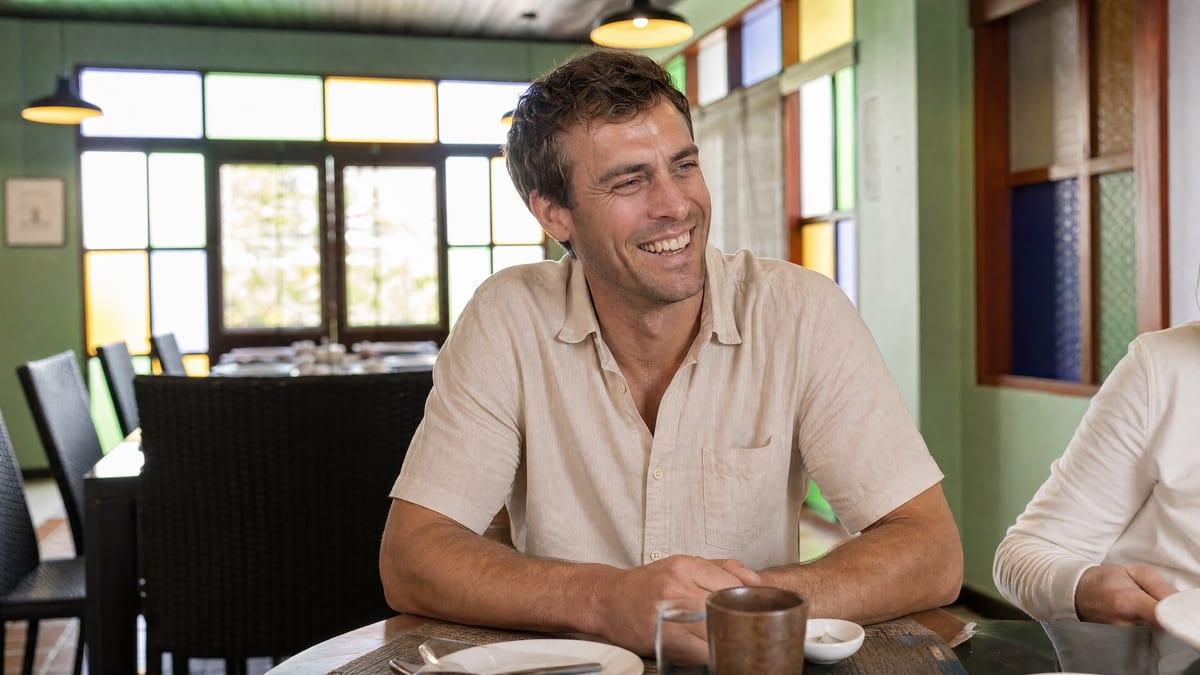 Man laughing at a shared dining table in a stained-glass dining room at Jintara Rehab Chiang Mai