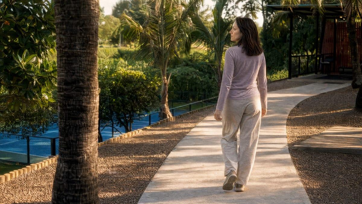 Woman walking a garden path lined with palms in warm afternoon light at a Chiang Mai rehab