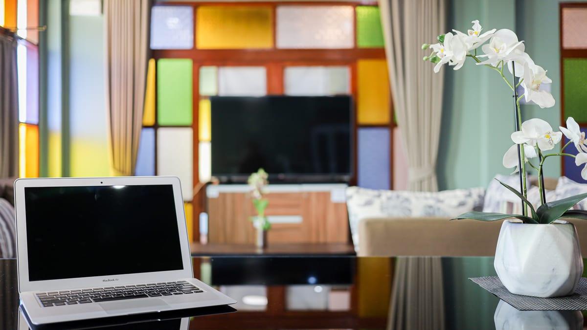 A laptop and orchid on a glass table in a stained-glass lounge at Jintara Rehab in Chiang Mai