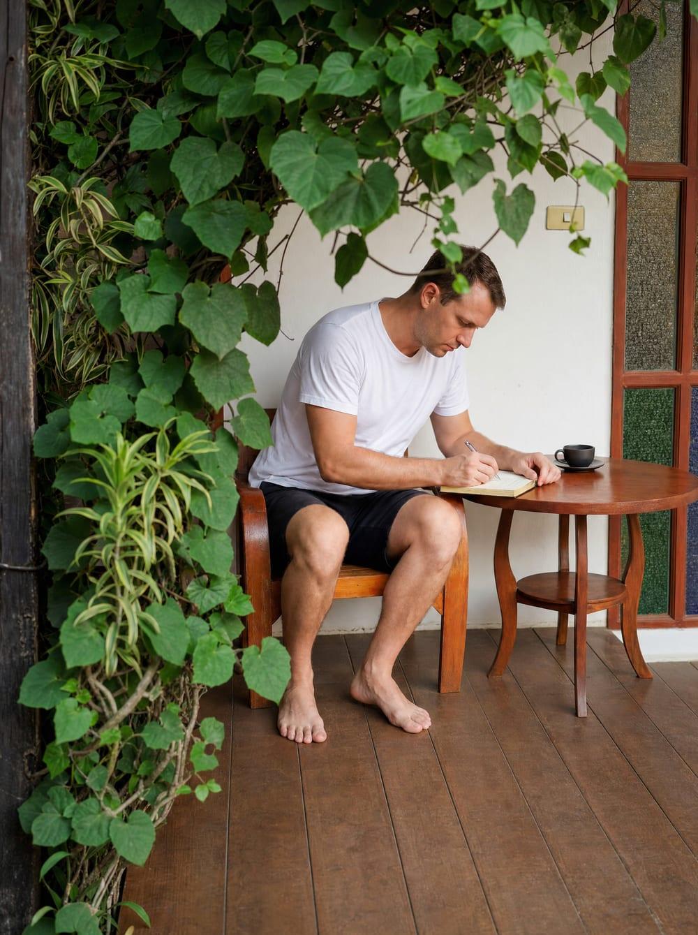 Man journaling at a timber table on a vine-framed veranda at Jintara Rehab Chiang Mai