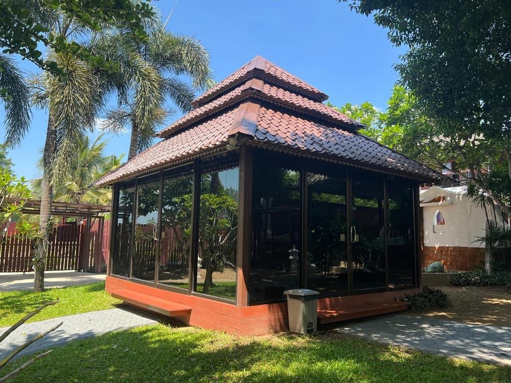 A glass-walled Lanna-style therapy pavilion surrounded by palm trees at Jintara Rehab Chiang Mai