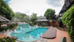 Jintara Rehab pool courtyard with teak buildings and lounge chairs in bright daytime, residential addiction treatment in Chiang Mai Thailand