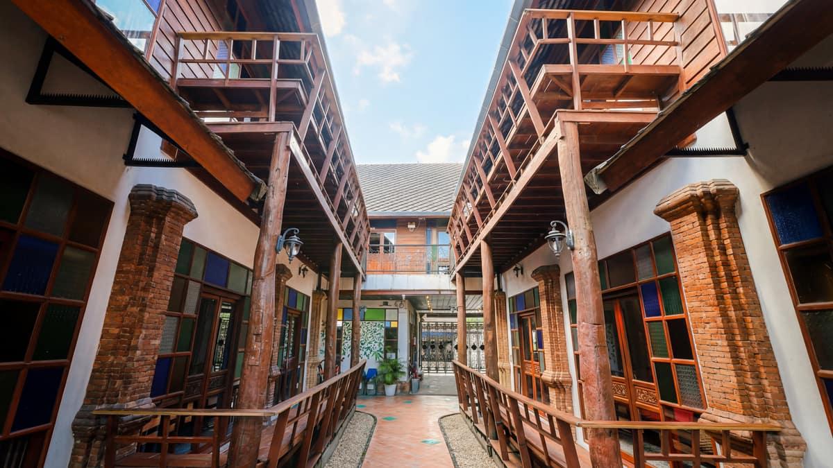 Symmetrical teak building corridor at Jintara Rehab Chiang Mai, showing the residential compound in bright daytime