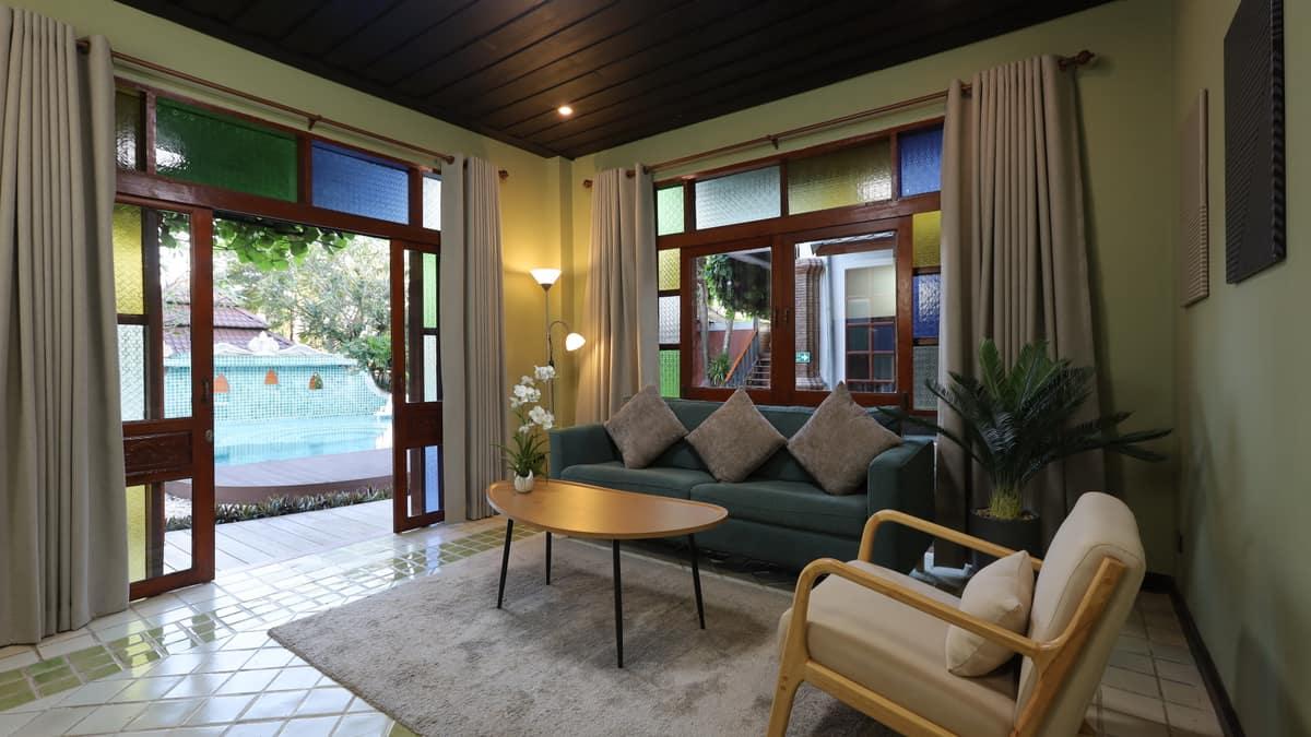 Warm lounge interior with teal sofa and French doors opening to the Jintara Rehab pool, Chiang Mai Thailand