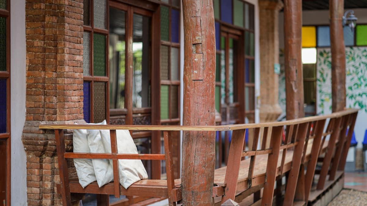 Teak veranda bench with tropical vines and stained-glass windows at Jintara Rehab Chiang Mai