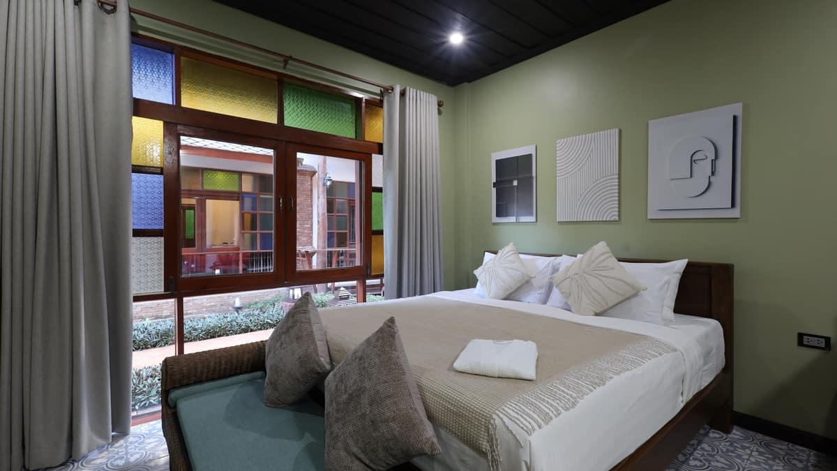 A private bedroom with a made bed and stained-glass window at Jintara Rehab Chiang Mai, where sleep is supported through cannabis withdrawal