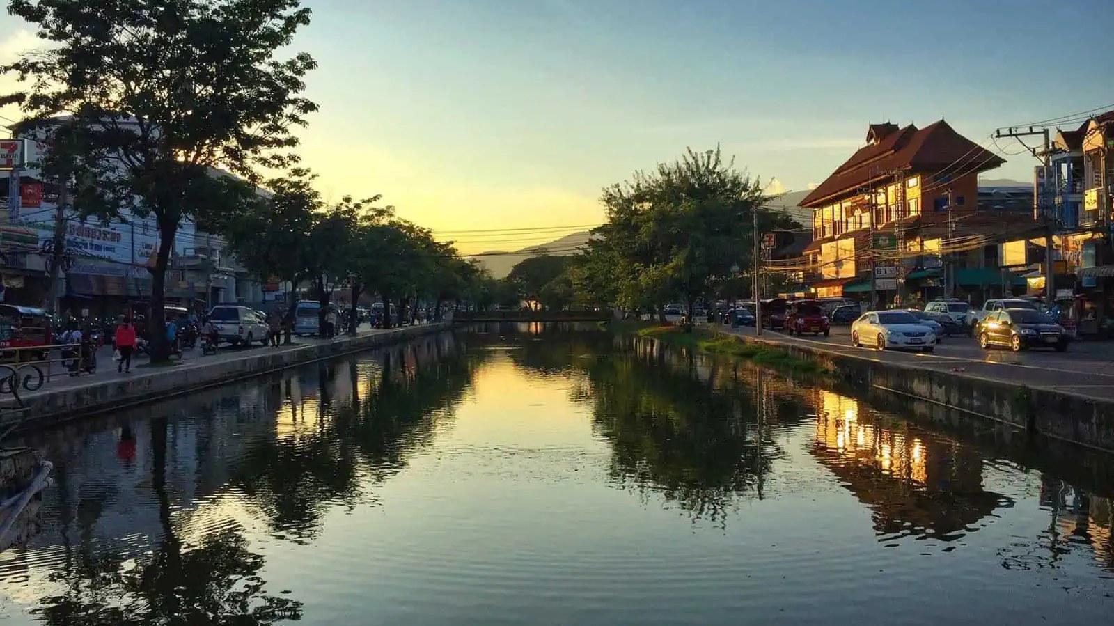 The Chiang Mai moat at dusk, with everyday traffic and shopfronts along both banks
