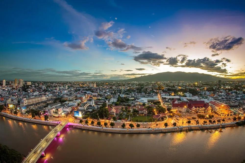 Aerial view of Chiang Mai at sunset, the river in the foreground and the mountains behind the city