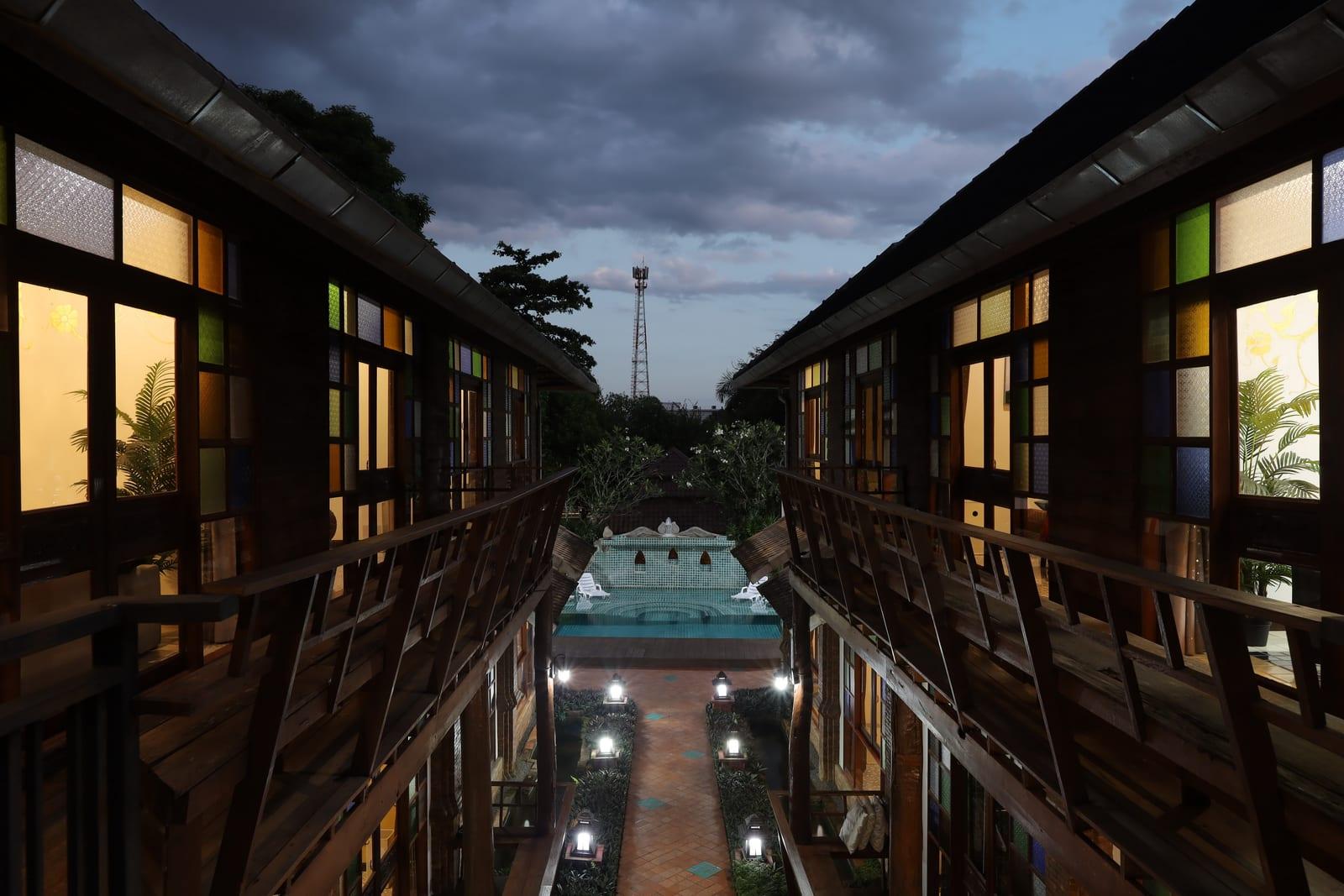 The two Lanna building wings at Jintara Rehab in Chiang Mai at dusk, with lantern-lit path and pool between them