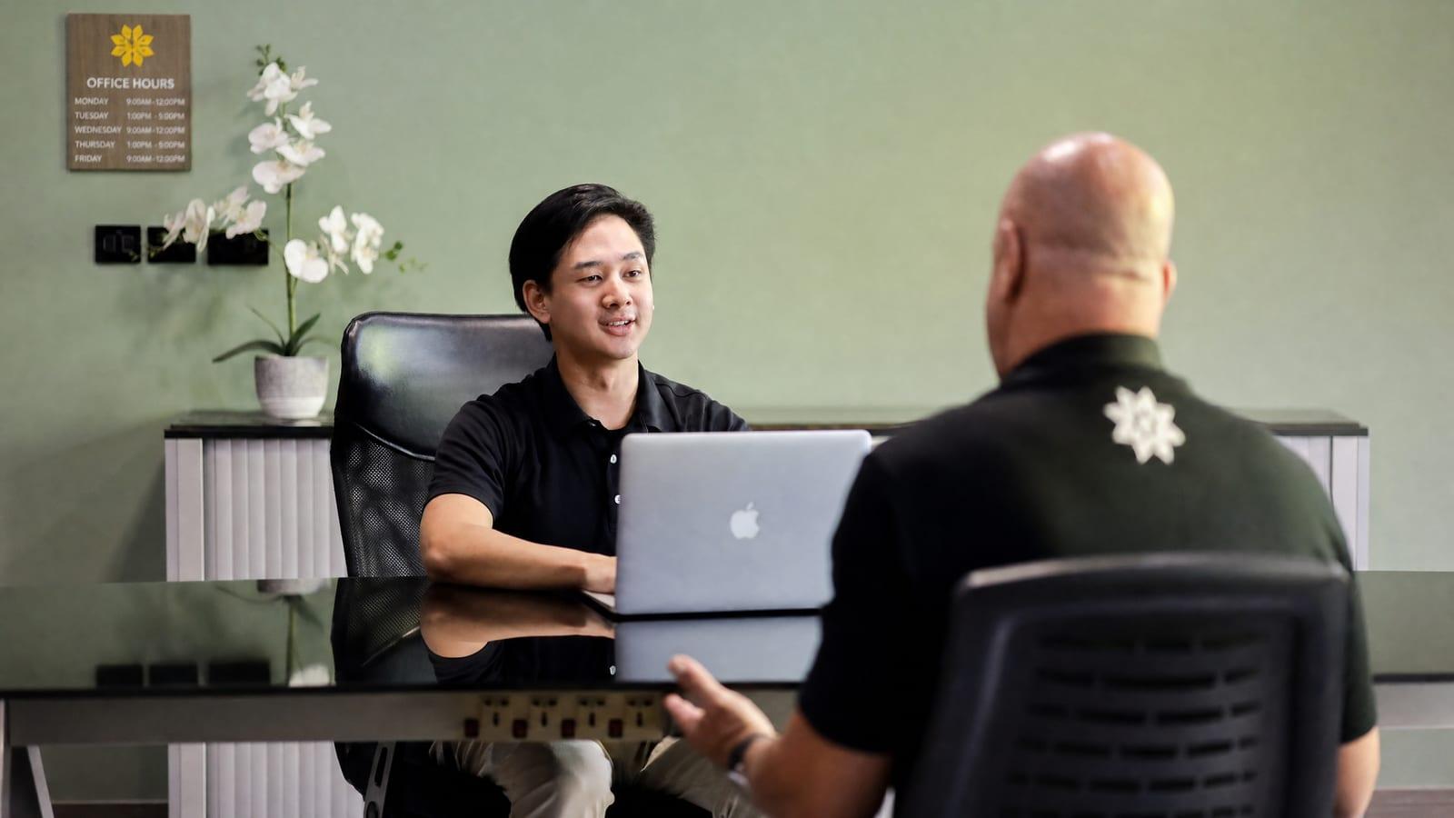 Young clinician at laptop in conversation with a client across the desk at Jintara Rehab Chiang Mai for cocaine and alcohol treatment planning