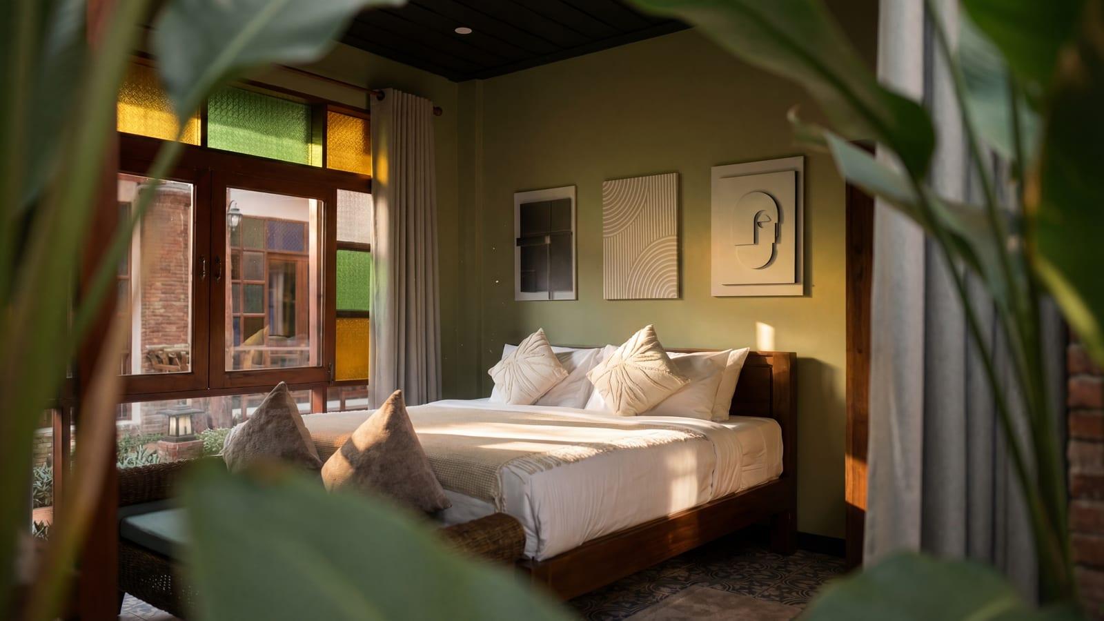 Sunlit sage-green private bedroom with king bed, warm morning light through stained glass at Jintara Rehab Chiang Mai for the closing chapter of cocaine and alcohol recovery