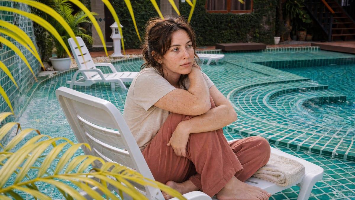 A young woman sits with one knee up on a pool lounger, looking out over the water at Jintara rehab in Chiang Mai