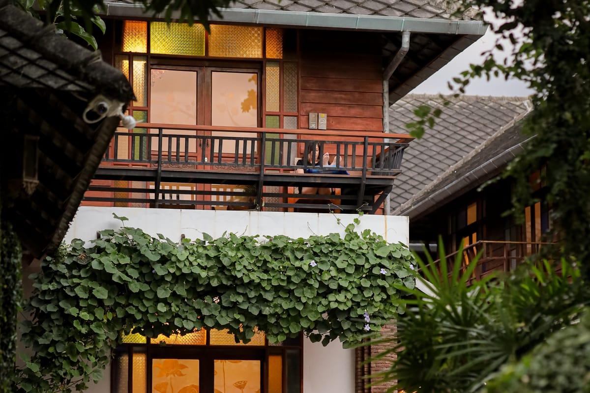 Lanna-style building at Jintara Rehab Chiang Mai viewed through tropical foliage with stained glass windows lit at dusk