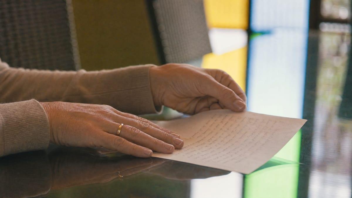 A woman's hands rest on a glass table beside a page of handwritten notes prepared before a family intervention