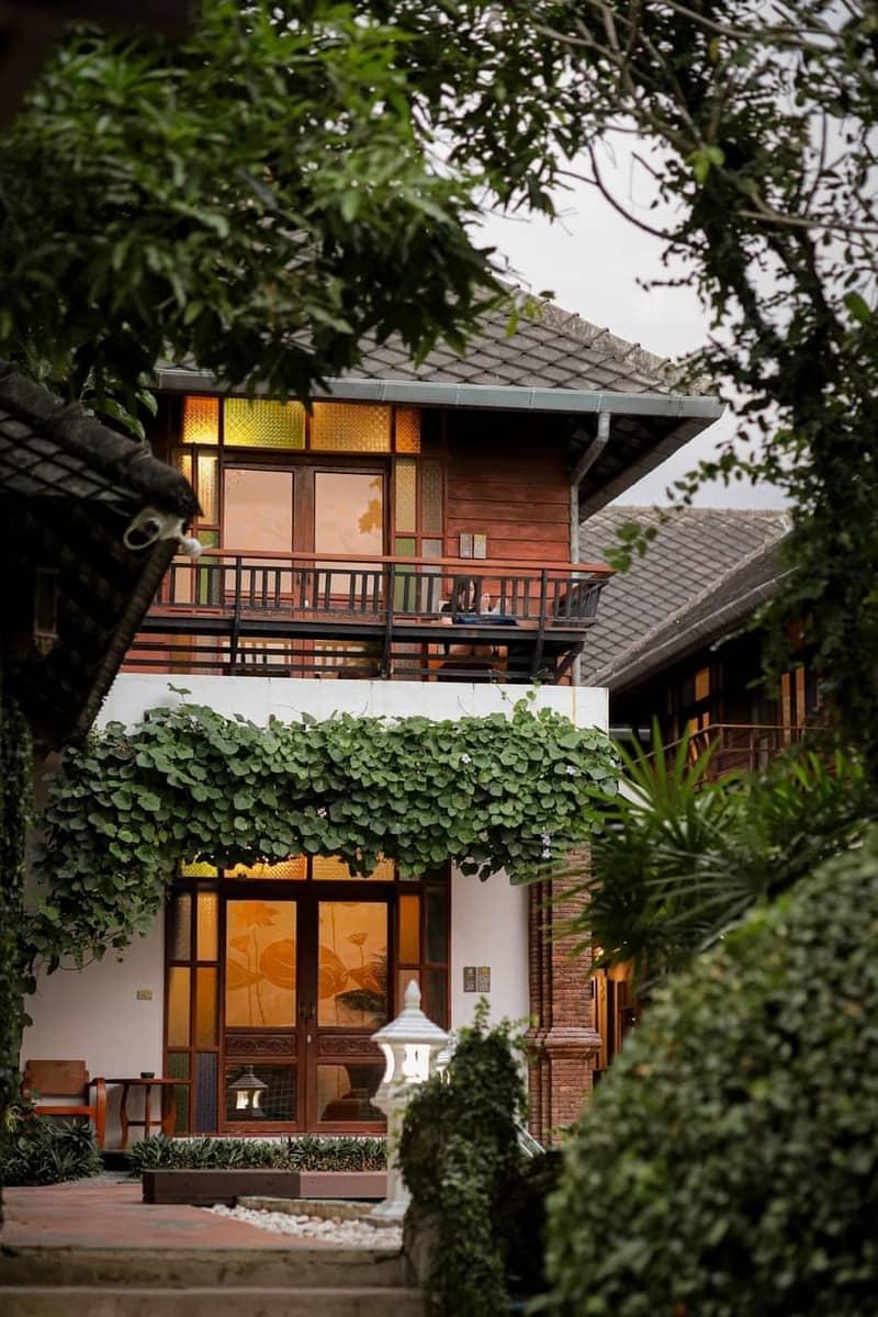 Two-storey Lanna-style building at Jintara Rehab in Chiang Mai photographed at dusk through tropical foliage