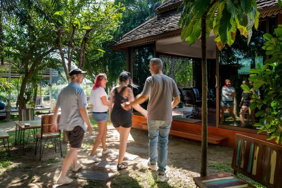 Individuals walking in tropical garden beside Lanna-style building at Jintara Rehab Chiang Mai