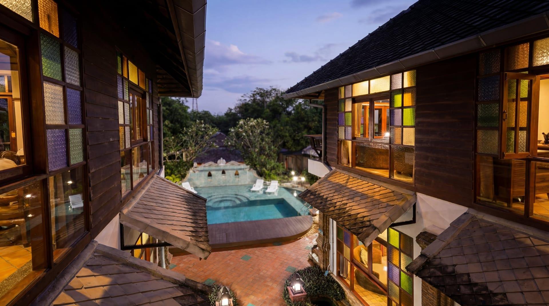 Teak buildings and stained glass windows around the pool at twilight at Jintara Rehab outside Chiang Mai