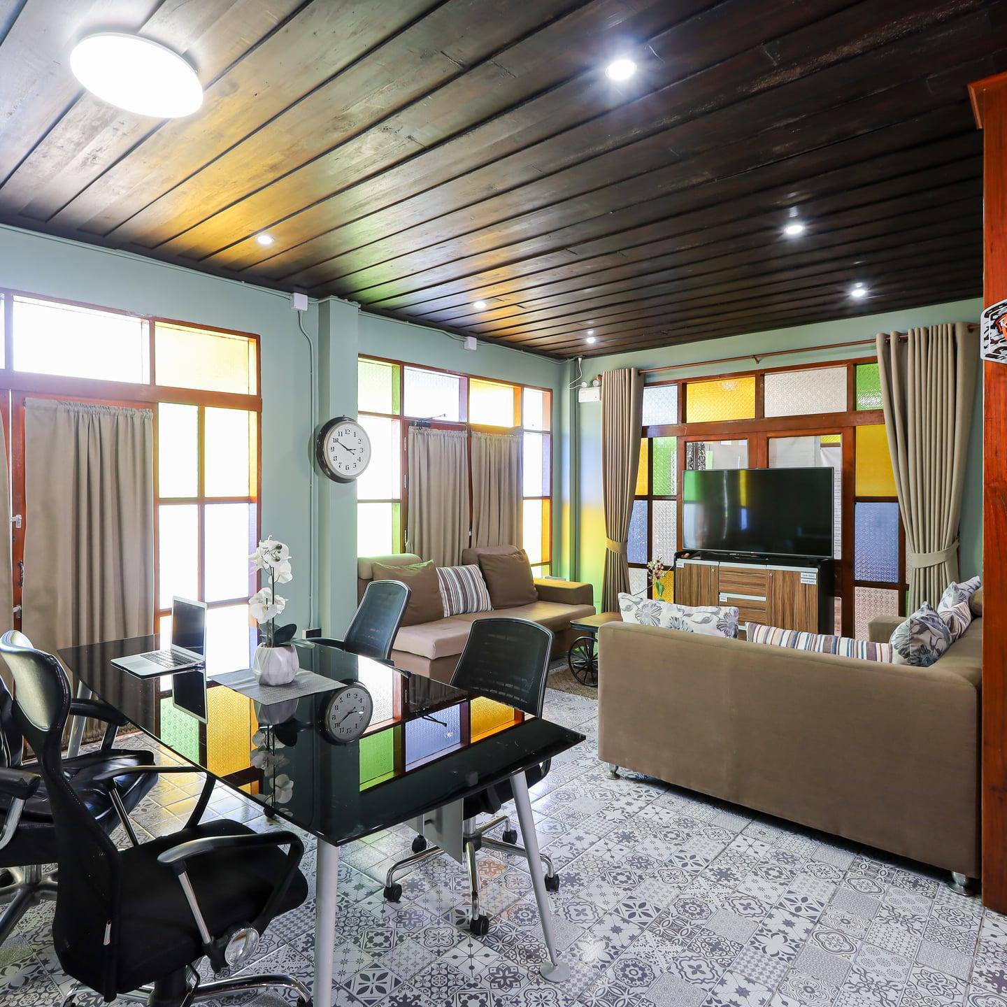 An empty lounge with pale sofas, a glass desk and coloured glass windows at Jintara Rehab