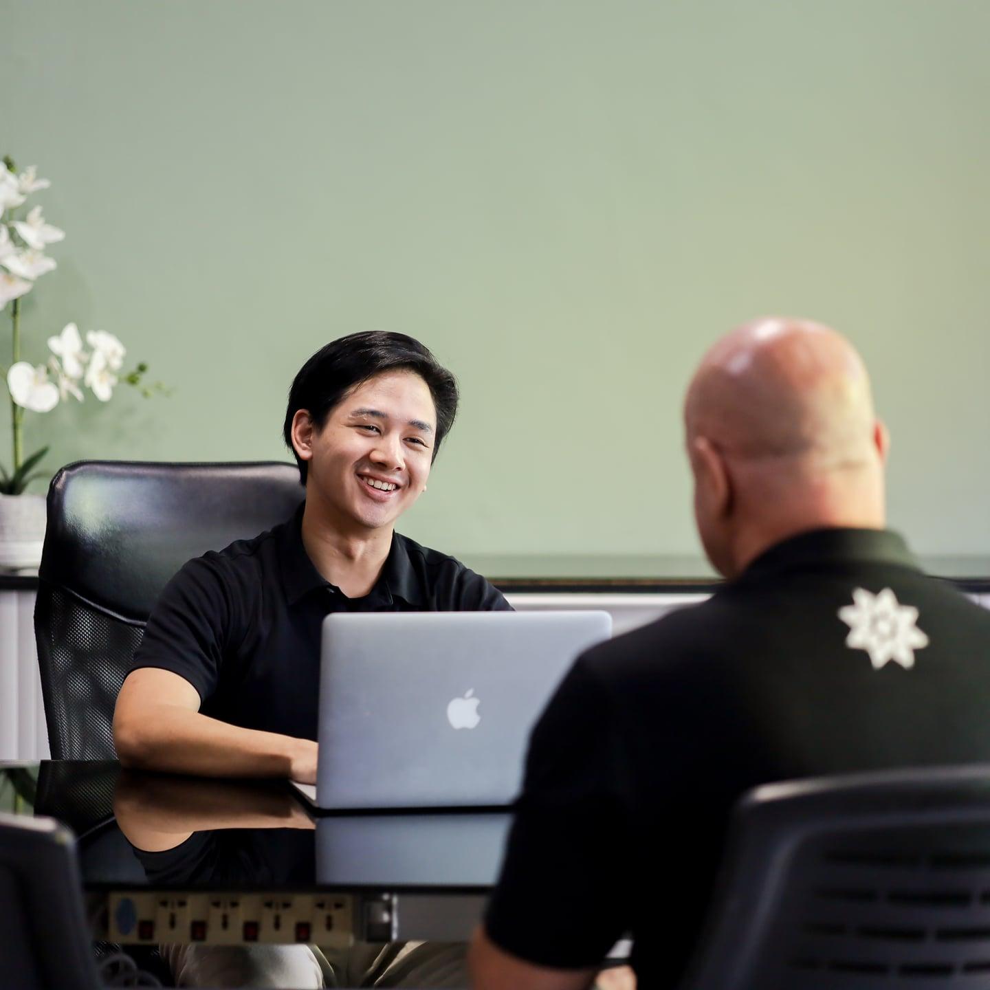 Two men talk across a desk in an office at Jintara Rehab in Chiang Mai
