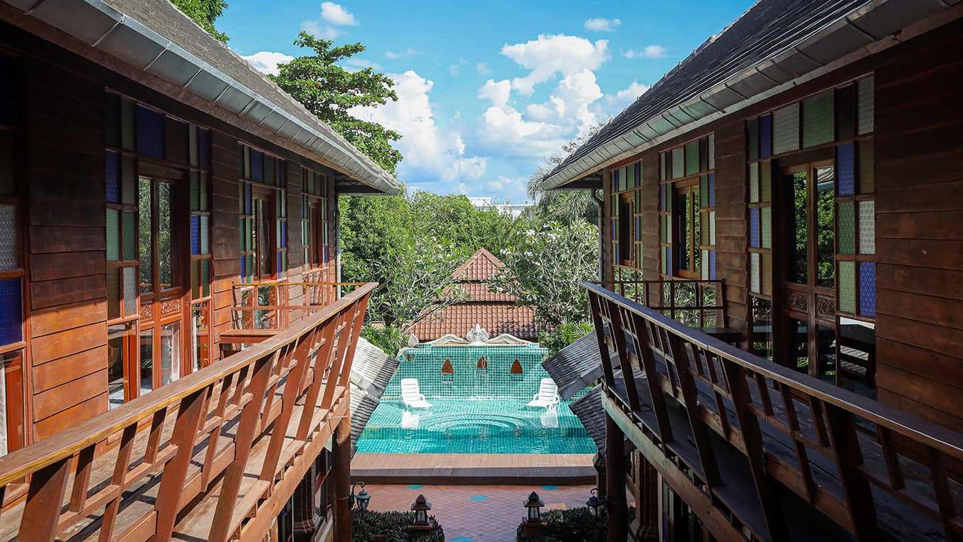 Teal mosaic pool and terracotta courtyard seen from a timber balcony walkway at Jintara Rehab Chiang Mai