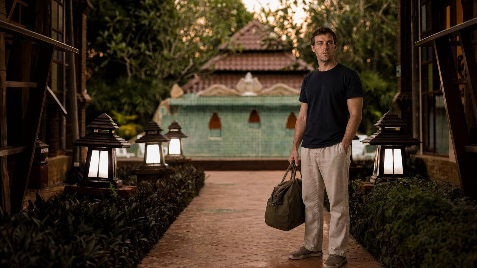 A Jintara client walks the lantern-lit timber walkway into the facility in Chiang Mai with his bag in one hand at the end of the trip from New Zealand