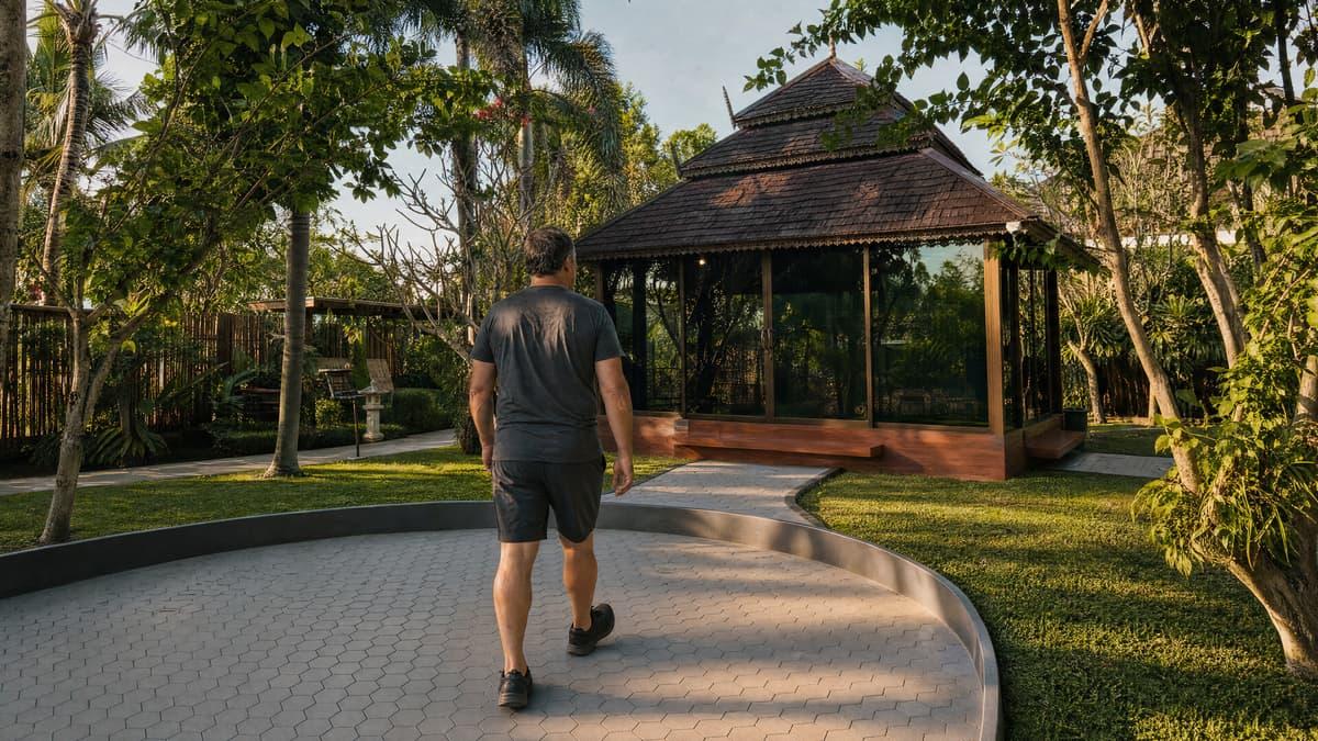 Client walking a wide step-free paved path through tropical grounds at a Chiang Mai rehab