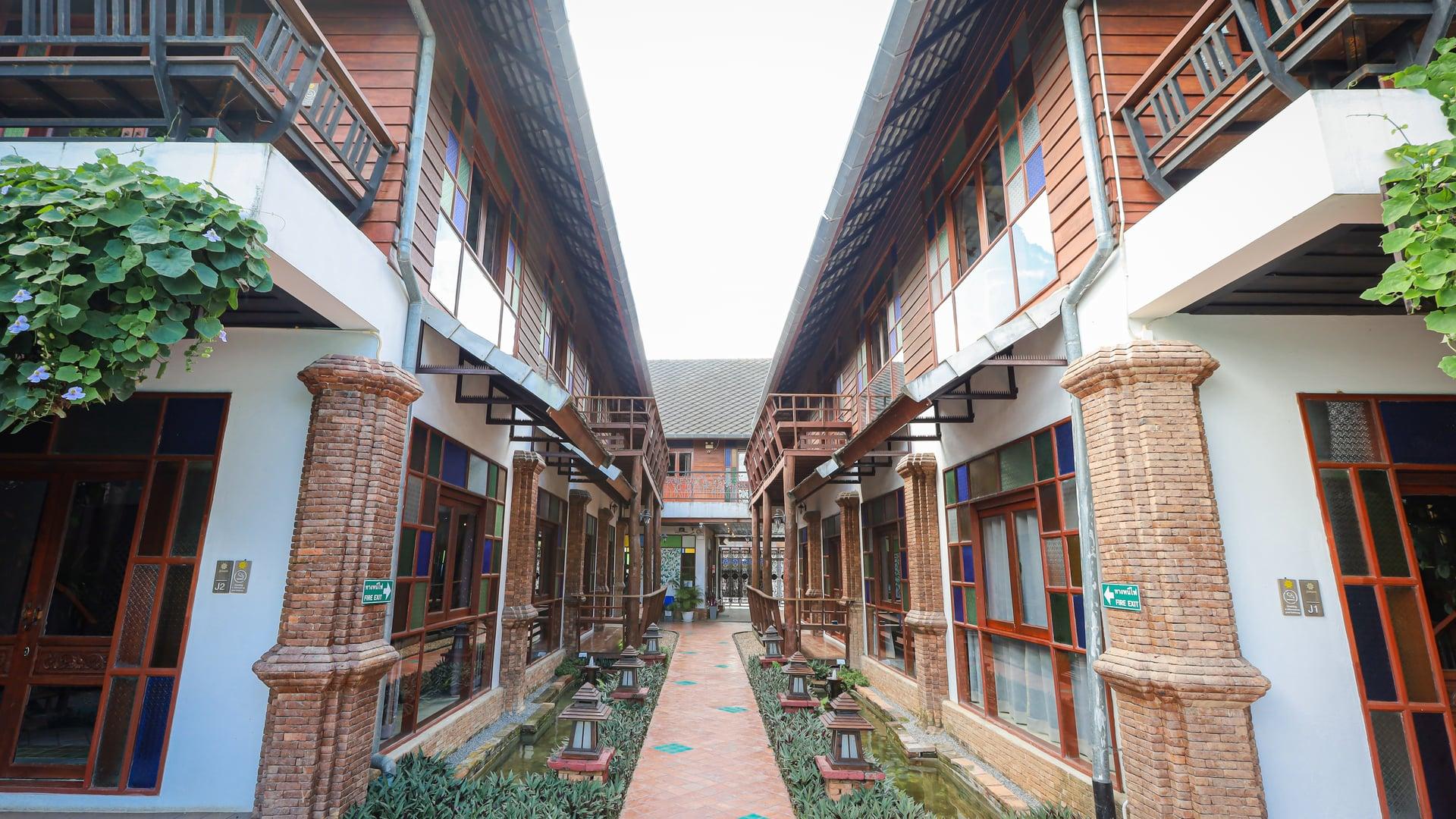 Brick walkway between timber buildings with balconies and coloured glass windows at Jintara Rehab