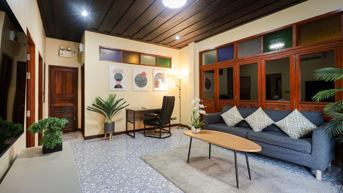 Empty sitting room with a blue-grey sofa, oval table, desk and plants at Jintara Rehab