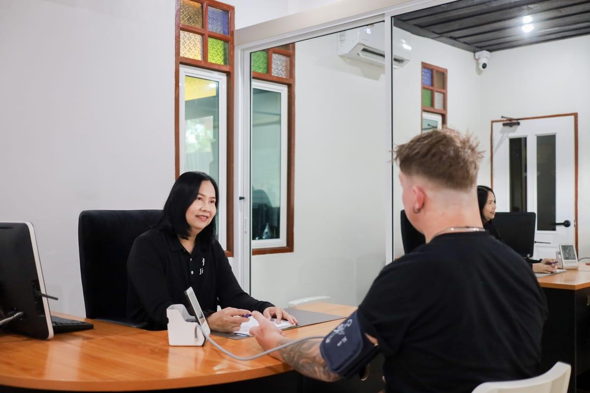 Nurse conducting client assessment at clinical desk with BP monitoring at Jintara Rehab Chiang Mai
