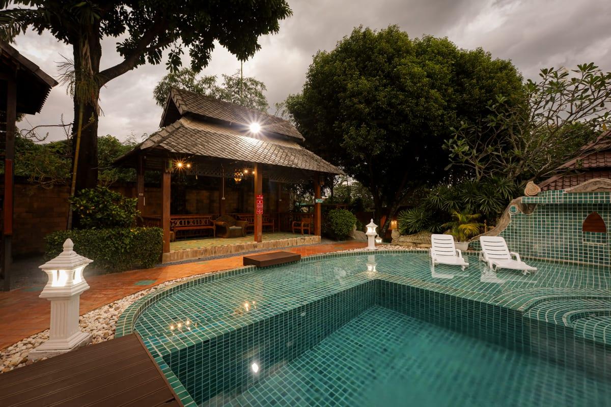 Evening view of turquoise pool and Lanna pavilion with lounge chairs at Jintara Rehab Thailand