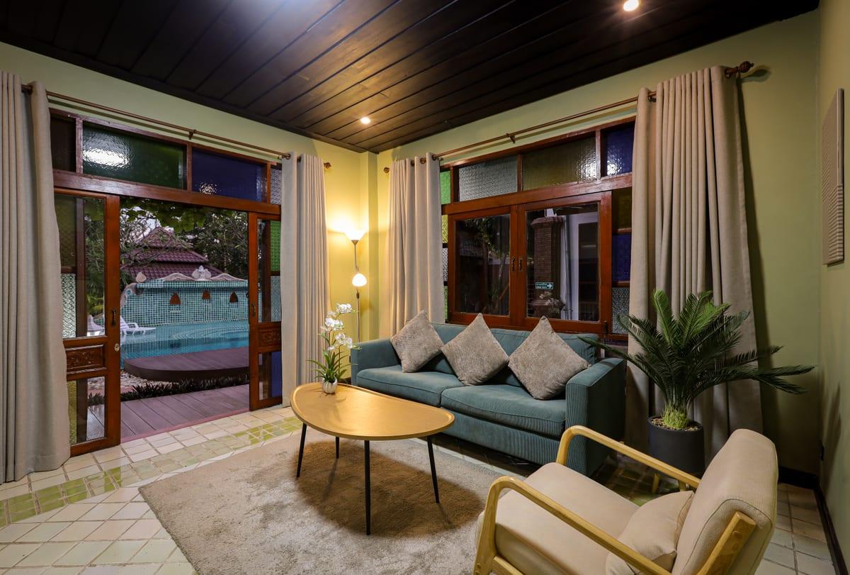 Warmly lit lounge with teal sofa and French doors opening to pool at Jintara Rehab Chiang Mai