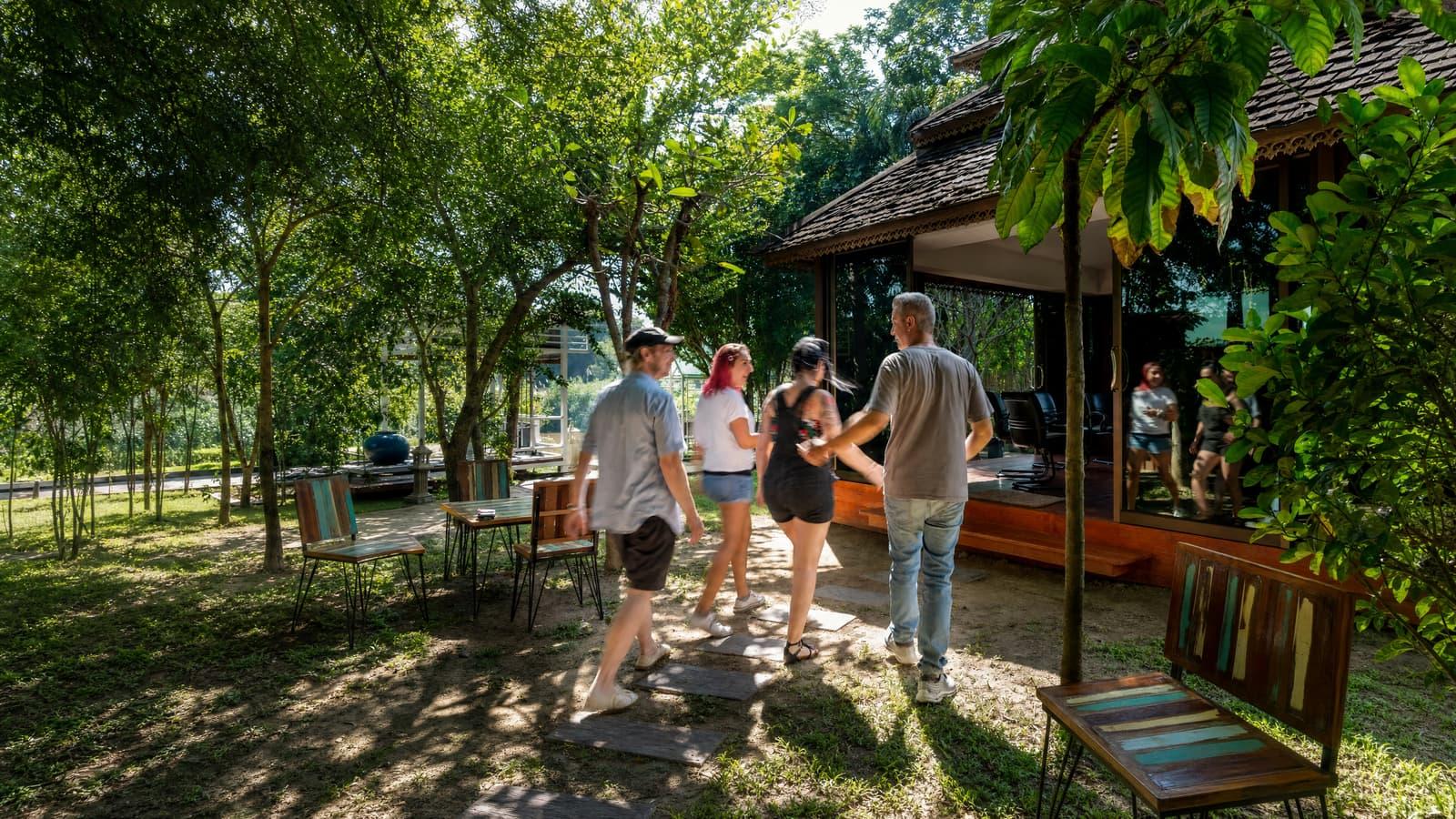 A small group walking a garden path toward a timber pavilion in dappled daylight