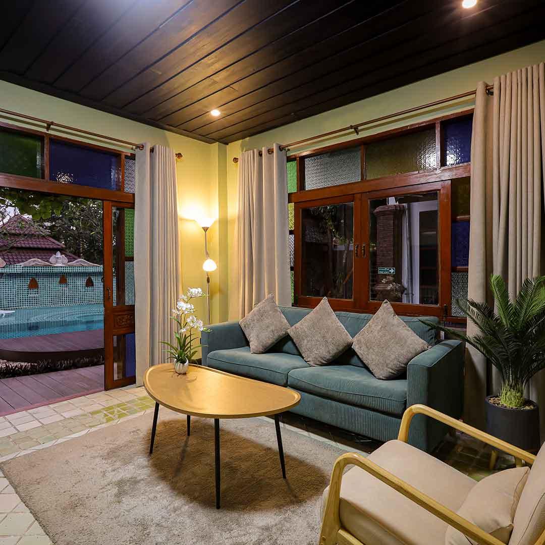 Private suite lounge with teal sofa and pool view through open doors at Jintara Rehab