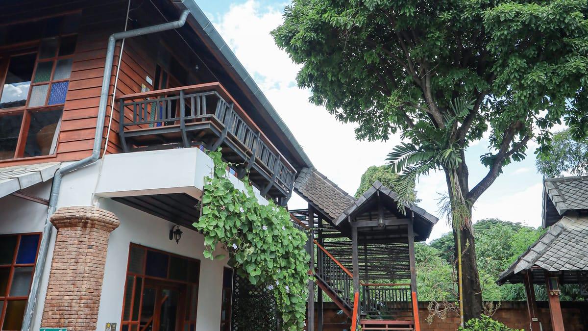 Teak accommodation building with a timber balcony, climbing vines and outside stairs at Jintara Rehab in Chiang Mai