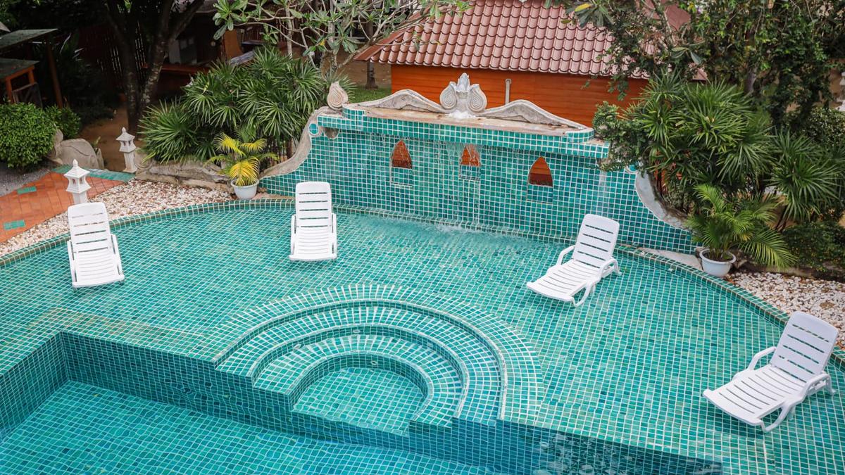 Pool with a tiled fountain wall and white loungers at Jintara Rehab in Chiang Mai