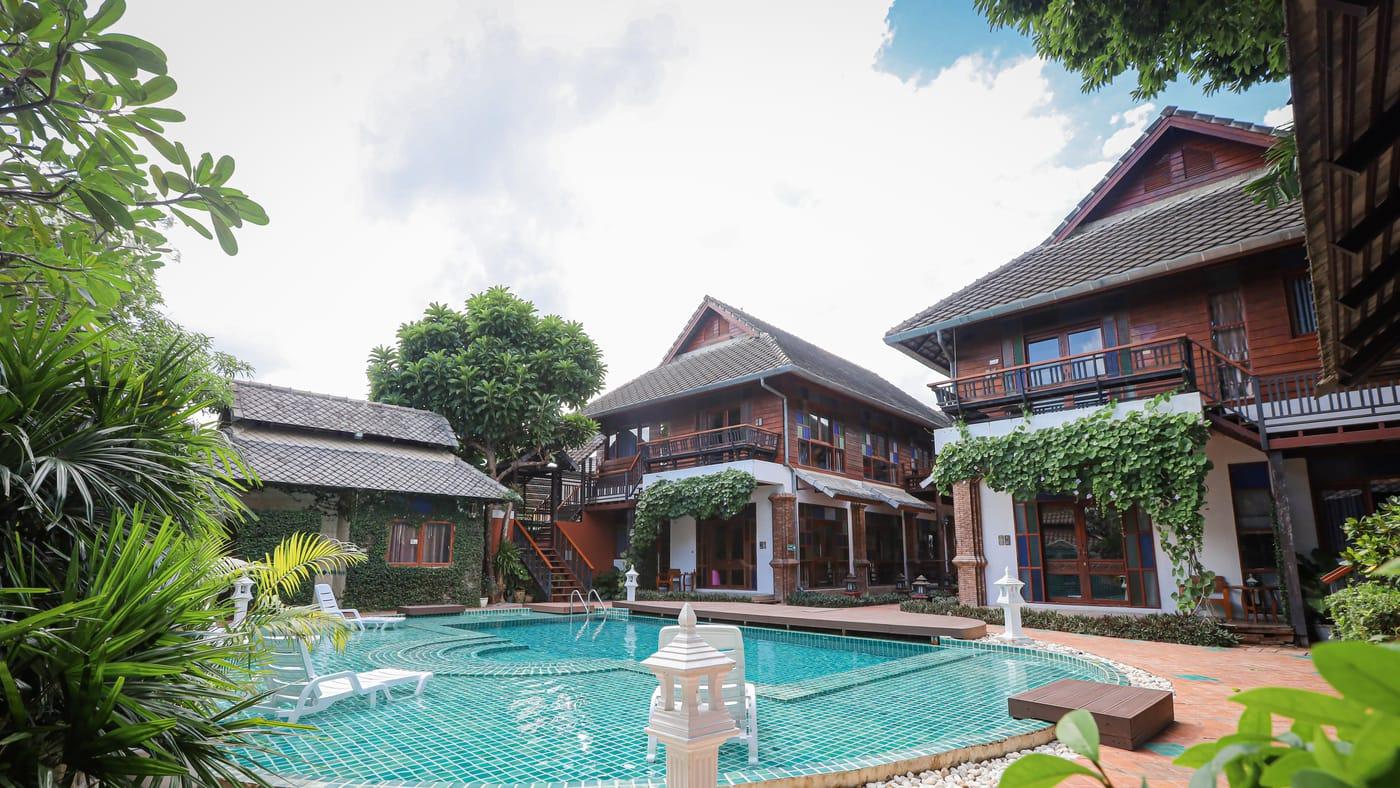 The pool and two-storey teak buildings at Jintara Rehab in Chiang Mai on a bright day, with vines over the ground-floor rooms