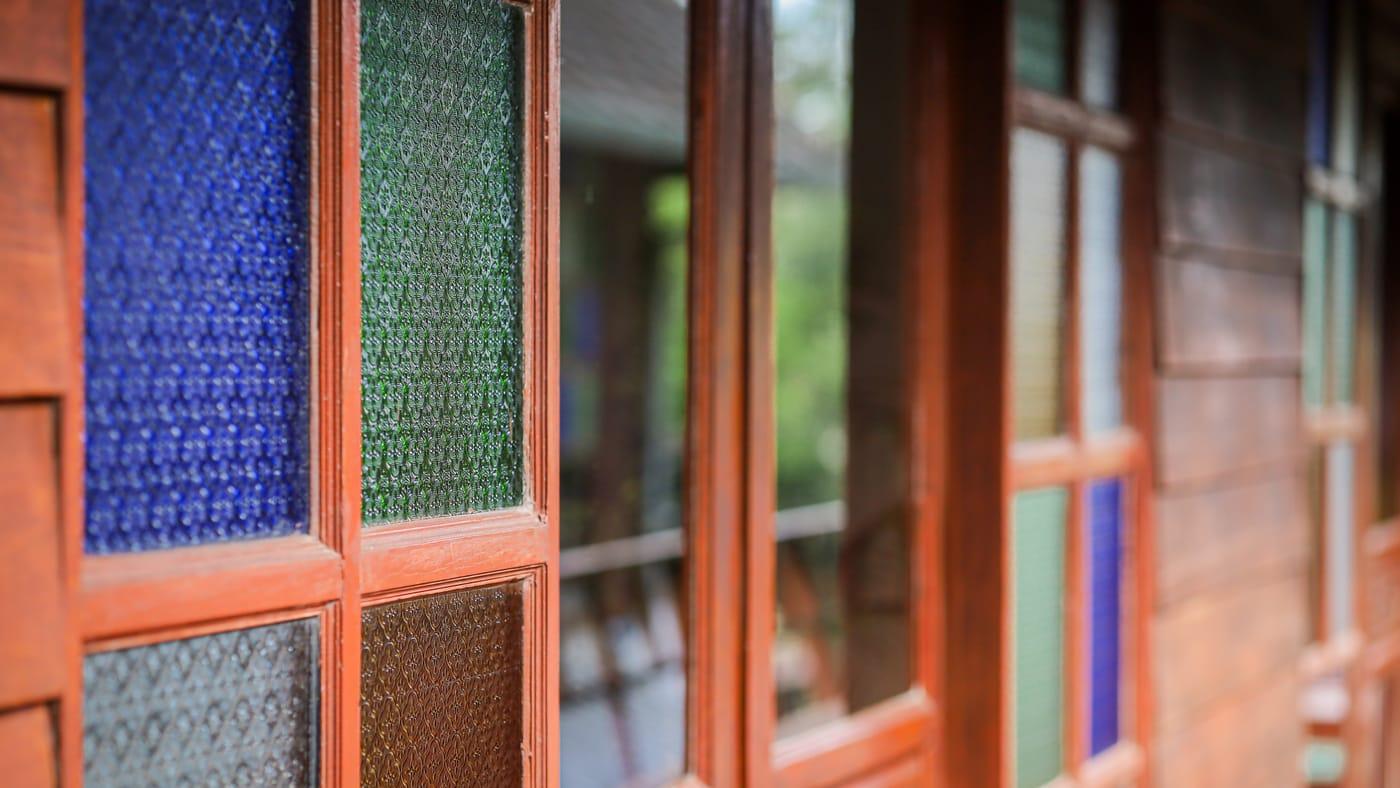 Blue and green stained glass in teak window frames at Jintara Rehab in Chiang Mai