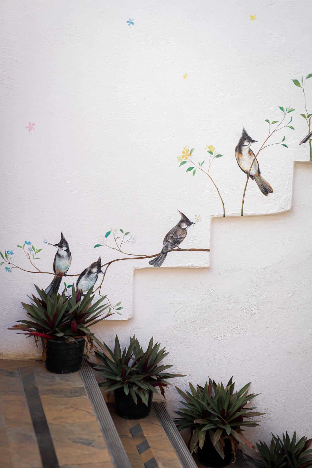 Painted birds and potted plants on a white stair wall at Jintara Rehab in Chiang Mai