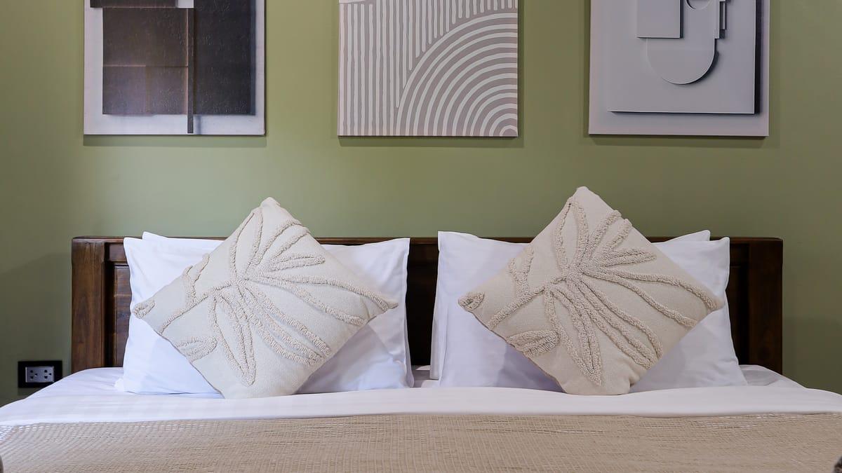 A made bed beneath white wall panels in a bedroom at Jintara Rehab in Chiang Mai