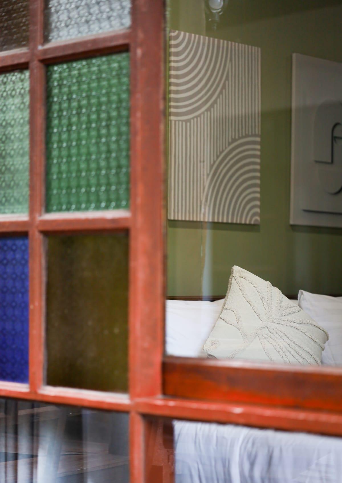 A bed with white pillows seen through a stained glass window at Jintara Rehab in Chiang Mai