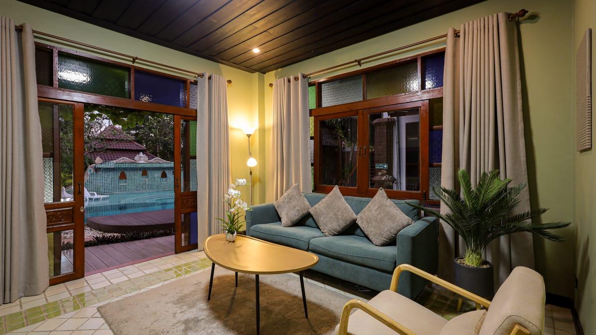 Lounge with a sofa and armchair, its doors open onto the pool, at Jintara Rehab in Chiang Mai