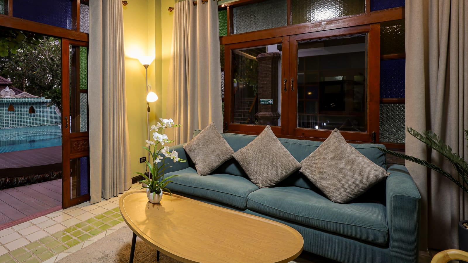 A sitting room with a sofa and coffee table, doors open to the pool, at Jintara Rehab in Chiang Mai