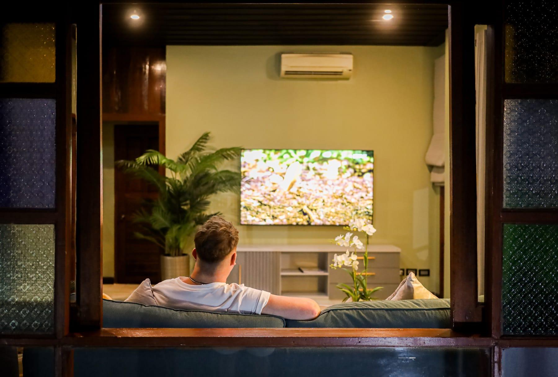 A man sits on a sofa watching television in a lounge at Jintara Rehab in Chiang Mai
