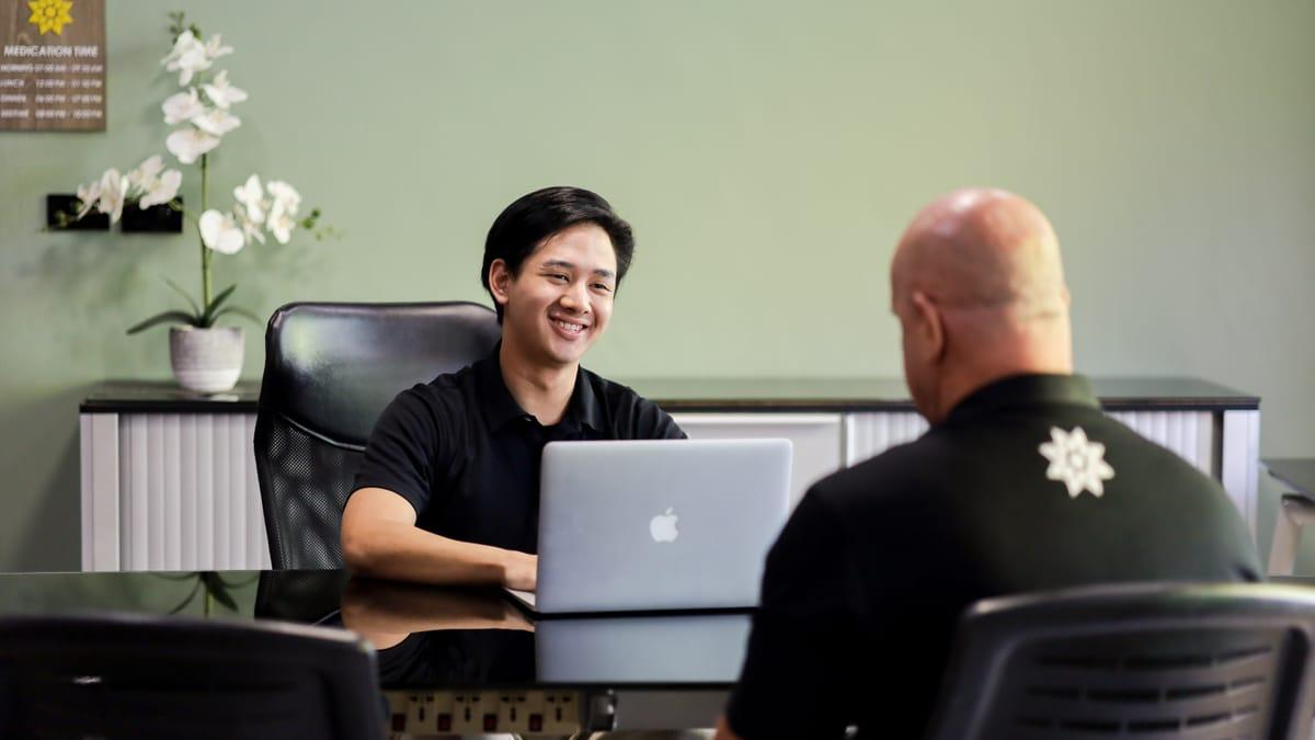 A Jintara staff member talks with a man across a desk in an office at Jintara Rehab in Chiang Mai