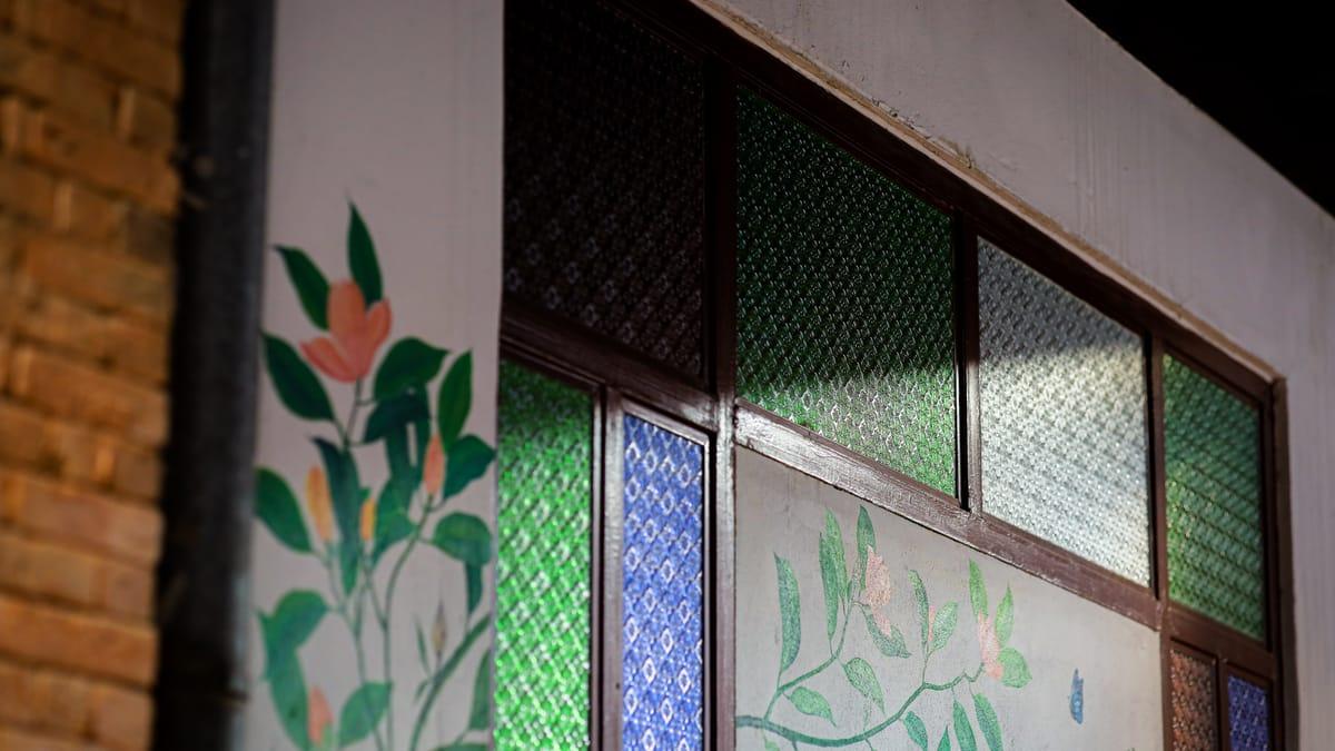 A painted flowering vine on a wall beside stained glass windows at Jintara Rehab in Chiang Mai