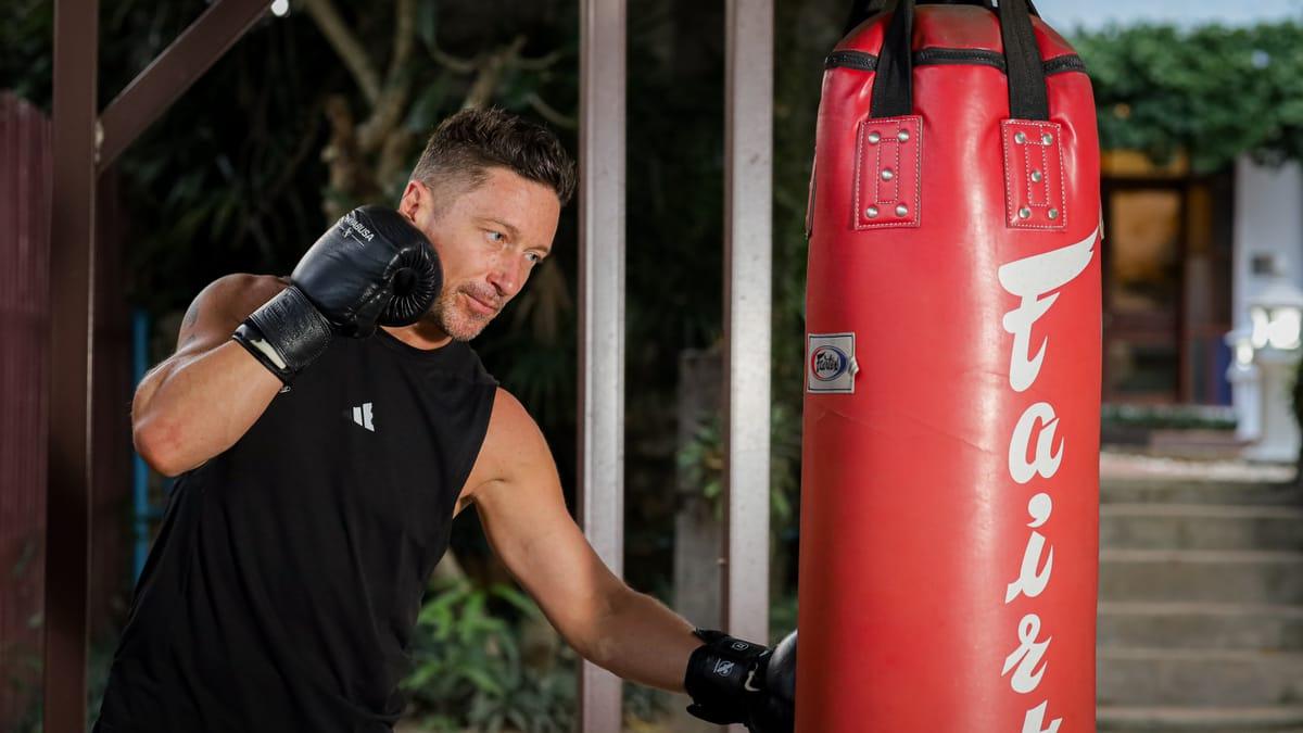 A man in boxing gloves working a red heavy bag in the garden at Jintara Rehab in Chiang Mai