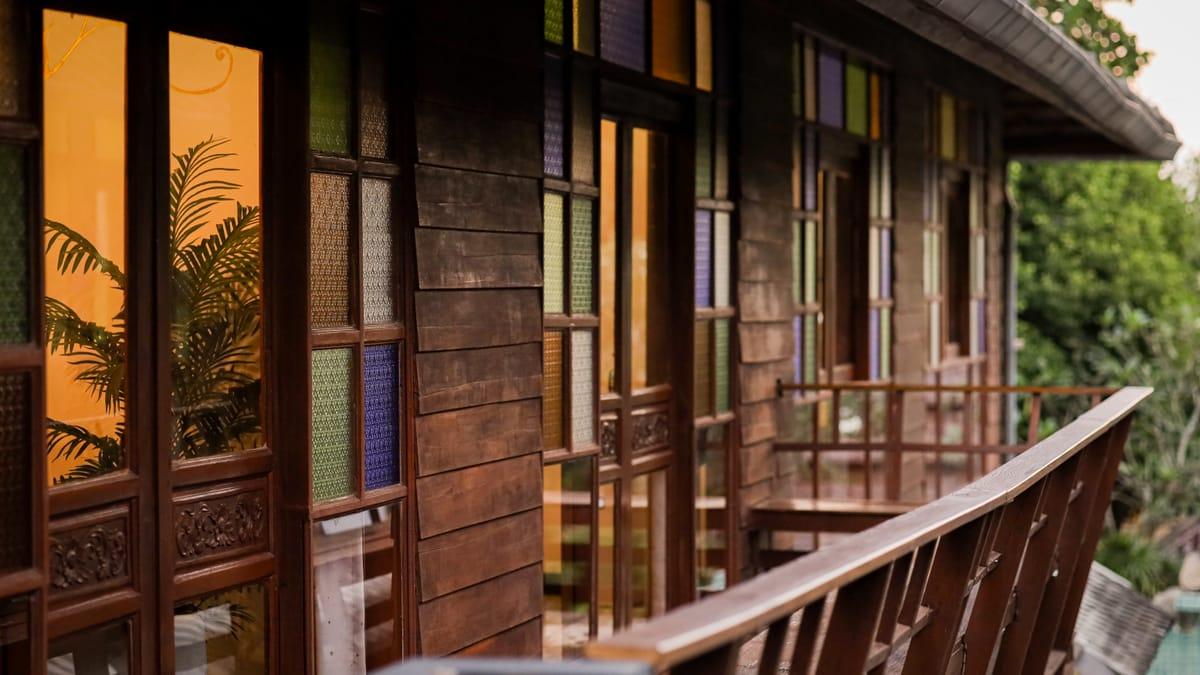 A teak balcony with stained-glass windows at Jintara Rehab in Chiang Mai