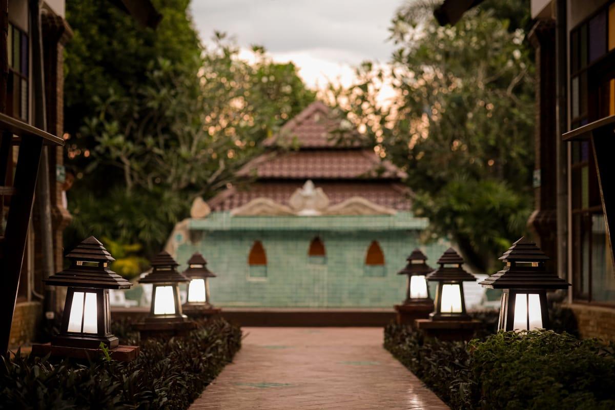 A lantern-lit garden path leading to the pool fountain at dusk at Jintara Rehab in Chiang Mai