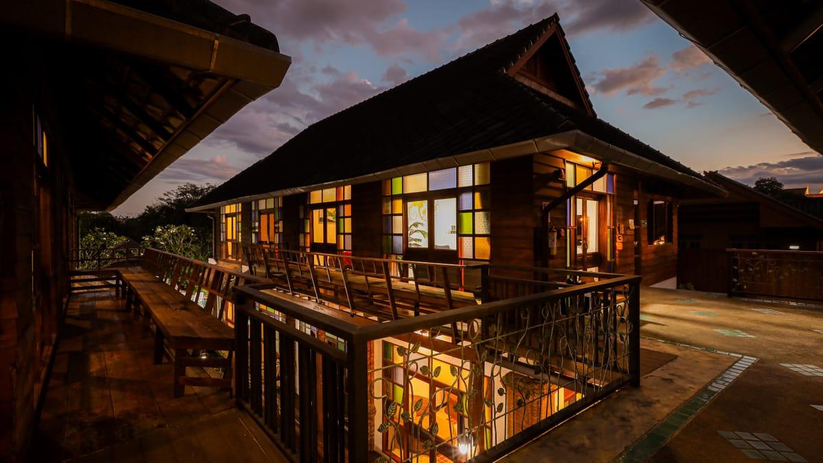 A teak building with its windows lit at dusk at Jintara Rehab in Chiang Mai
